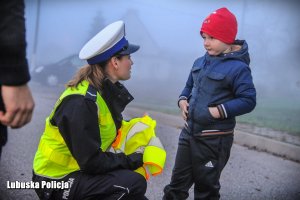 Policjantka zakłada dziecku kamizelkę odblaskową.